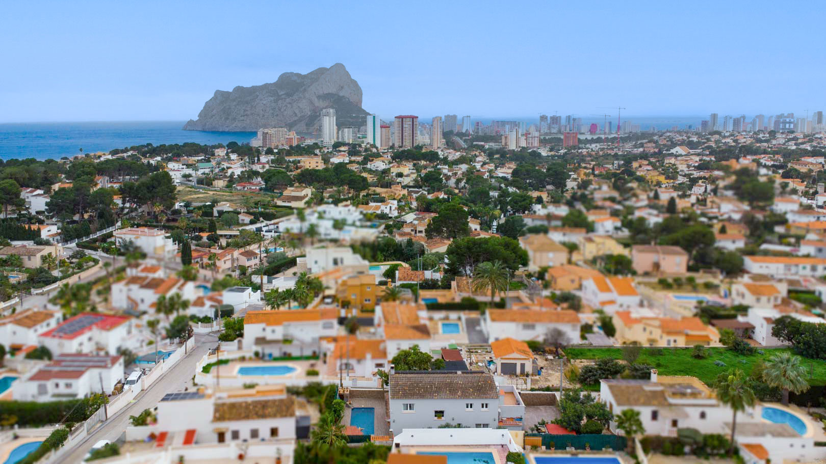 Vue aérienne panoramique du quartier résidentiel de Carrio à Calpe, avec le Peñón de Ifach et la mer Méditerranée en arrière-plan sous un ciel clair.