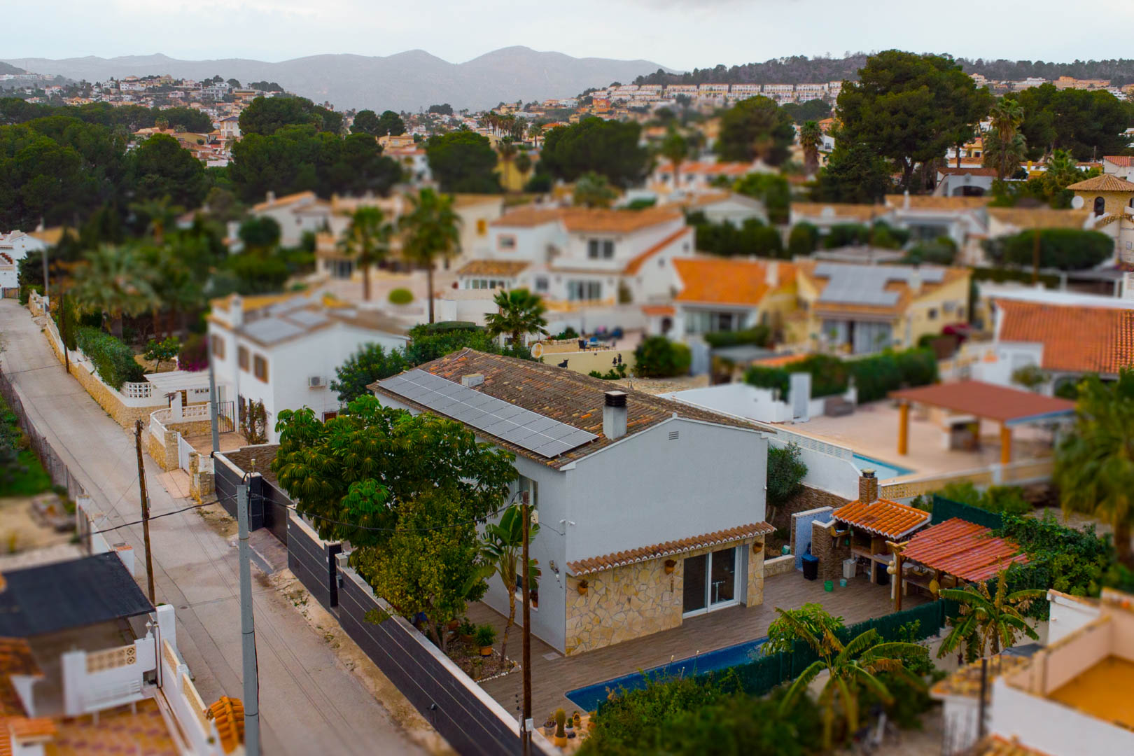 Vue surélevée de la villa avec panneaux photovoltaïques, piscine privée et espace barbecue extérieur, entourée par un paysage de montagnes.