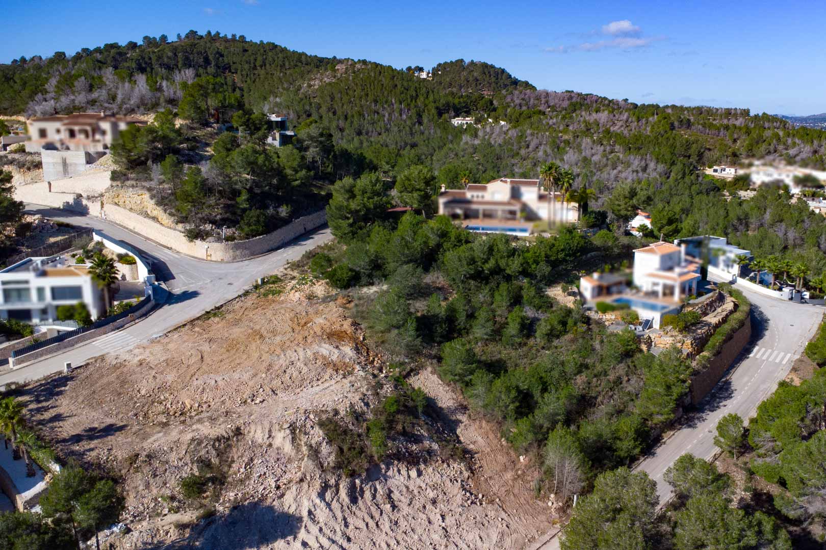 Terrain à bâtir en angle dans l'urbanisation Tosalet 5, entouré de pinèdes et de villas modernes, avec accès par routes goudronnées et topographie en pente.