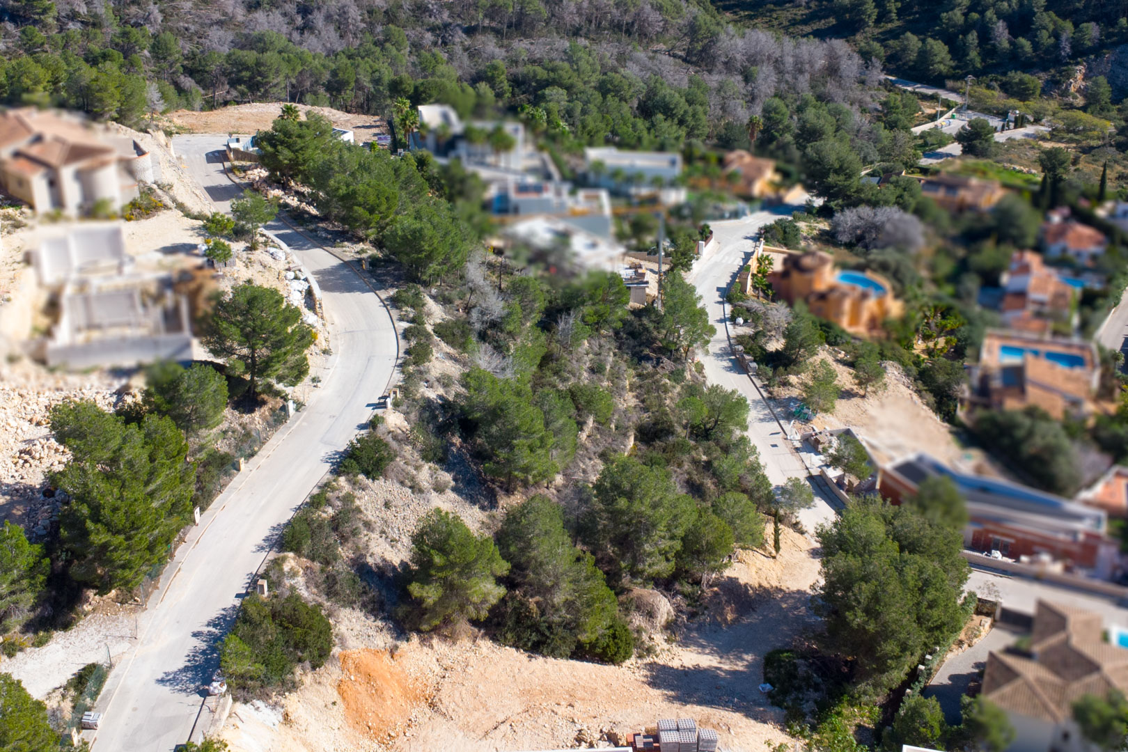 Vue aérienne de l'urbanisation Tosalet 5 à Jávea, illustrant les routes d'accès goudronnées, les terrains à bâtir en pente et la végétation méditerranéenne environnante.