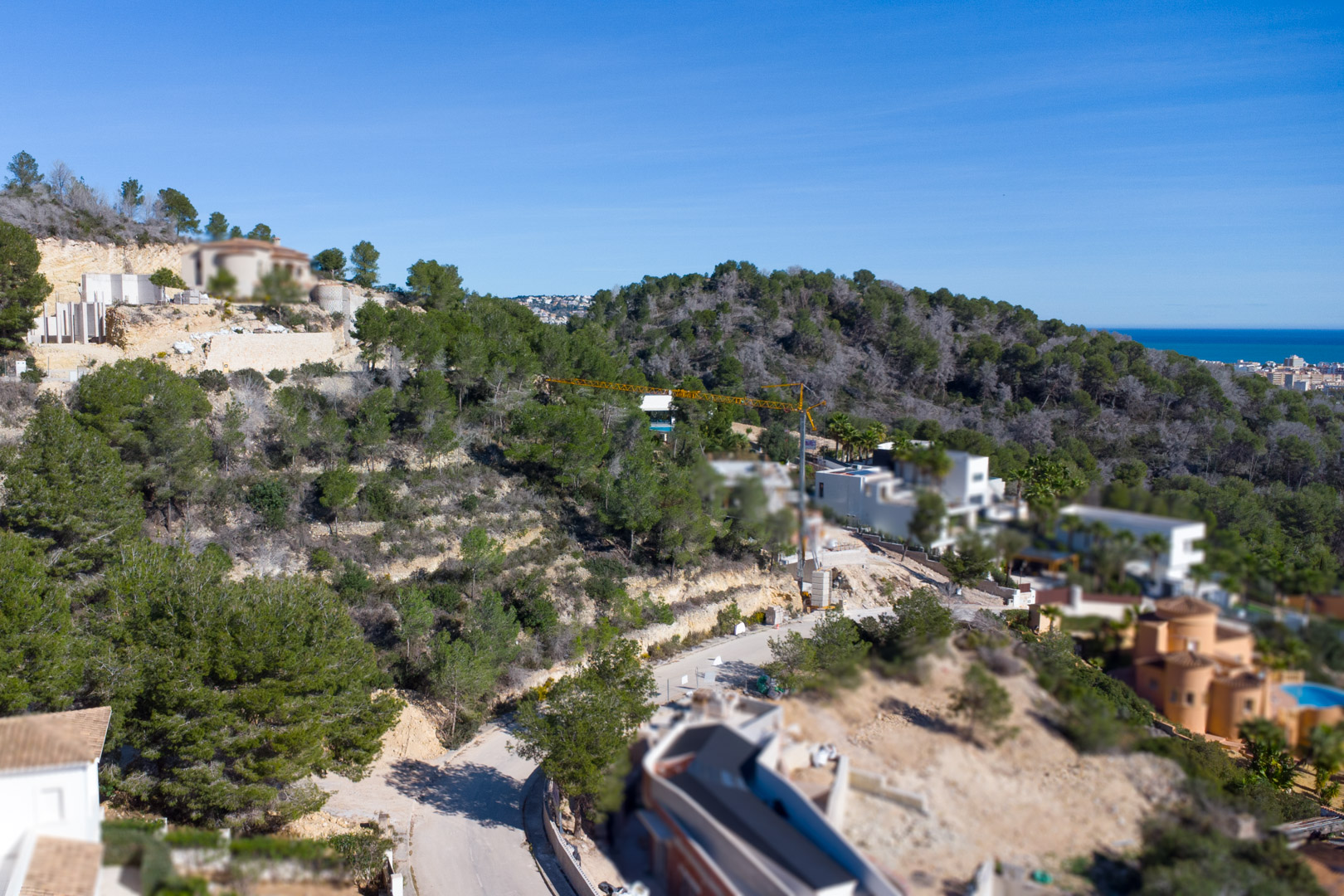 Vue aérienne de l'urbanisation Tosalet 5 à Jávea, présentant des terrains en pente entourés de pins avec une vue dégagée sur la mer Méditerranée.
