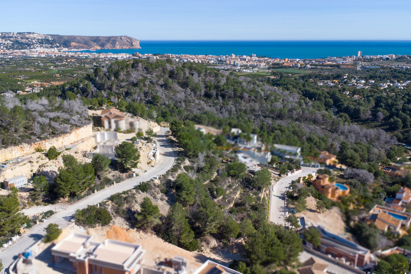 Vue aérienne du lotissement Tosalet 5 à Jávea, illustrant les parcelles en pente entourées de pins avec vue sur la mer Méditerranée et le Cabo de San Antonio.