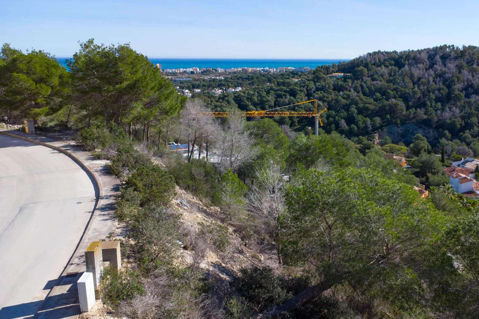 Vue panoramique depuis le terrain surélevé vers la mer Méditerranée, illustrant la végétation de pins et l'infrastructure routière de l'urbanisation Tosalet 5.