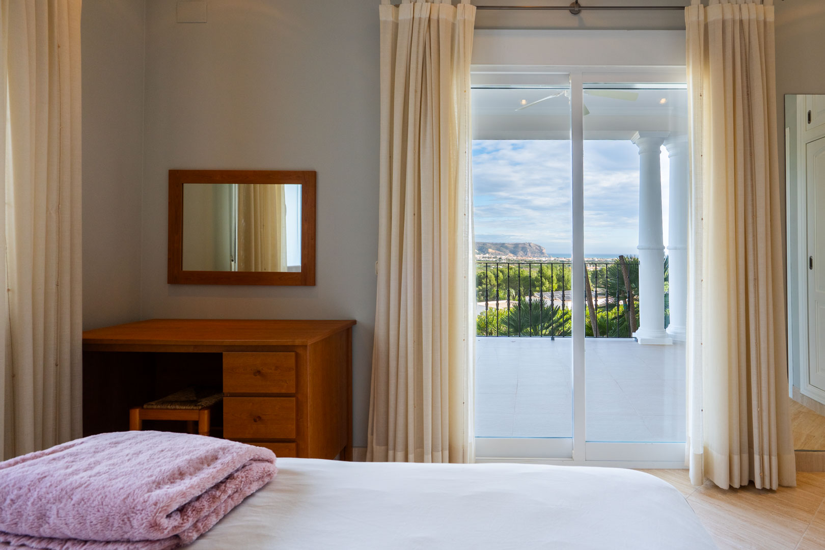 Chambre avec coiffeuse en bois et accès direct à une terrasse privée offrant une vue dégagée sur la mer et le massif du Montgó.