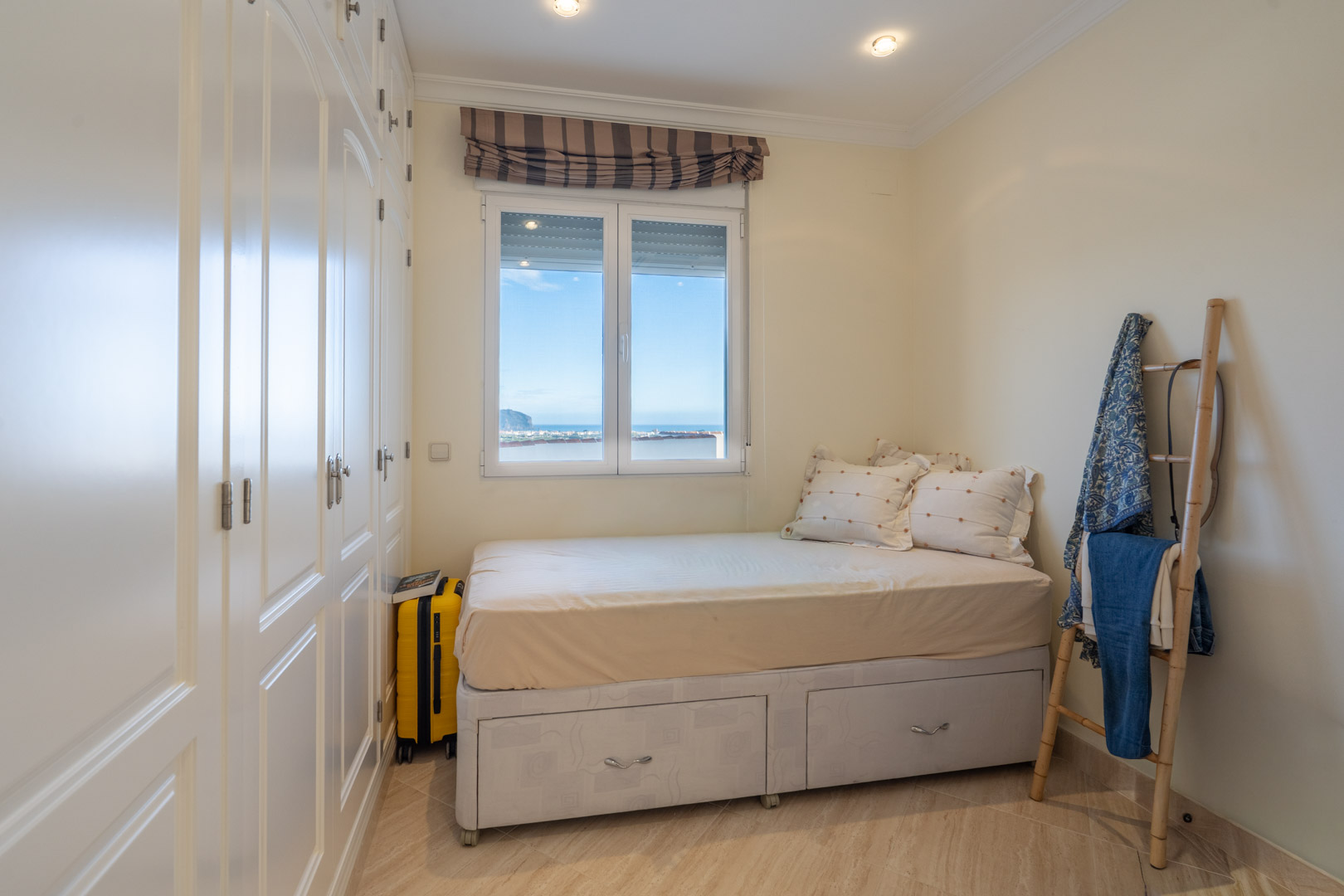 Chambre avec placards intégrés blancs, lit avec tiroirs de rangement et fenêtre offrant une vue dégagée sur la mer Méditerranée.