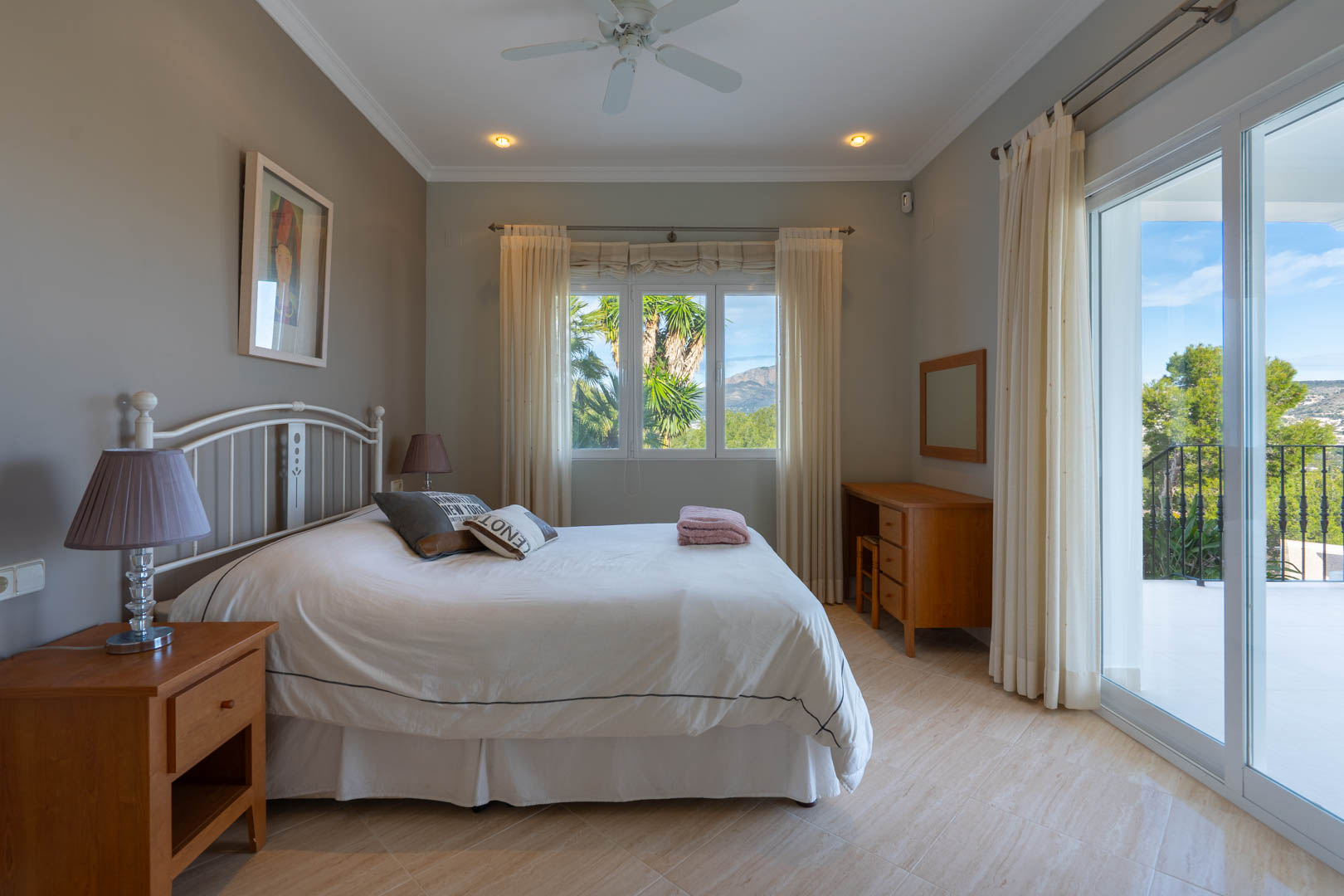 Chambre lumineuse avec sol en grès, mobilier en bois et accès direct à la terrasse offrant une vue dégagée sur le Montgó et la végétation.
