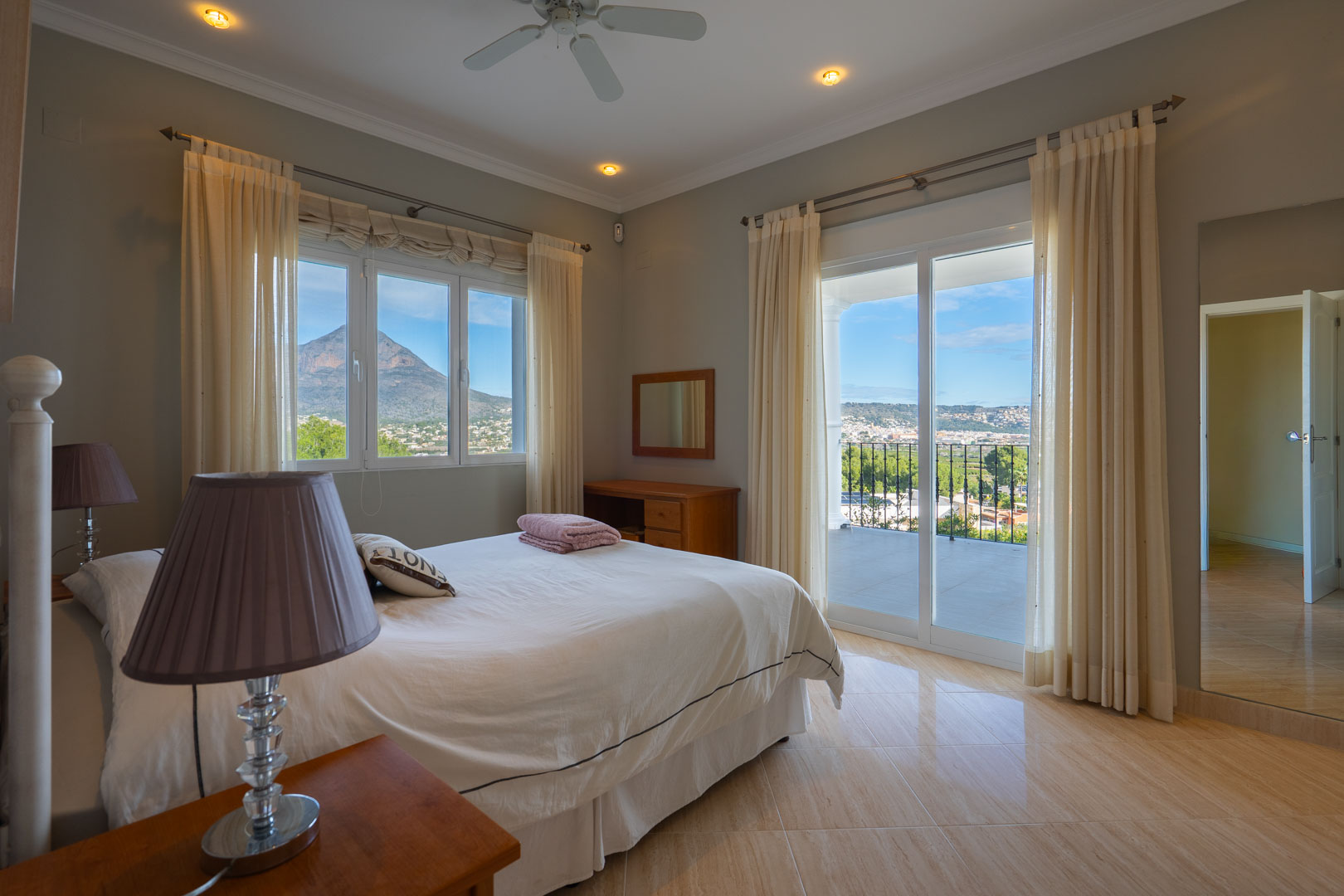 Chambre principale avec accès à une terrasse privée, vue panoramique sur le Montgó et sol en grès poli. Comprend un ventilateur de plafond et de grandes baies vitrées.