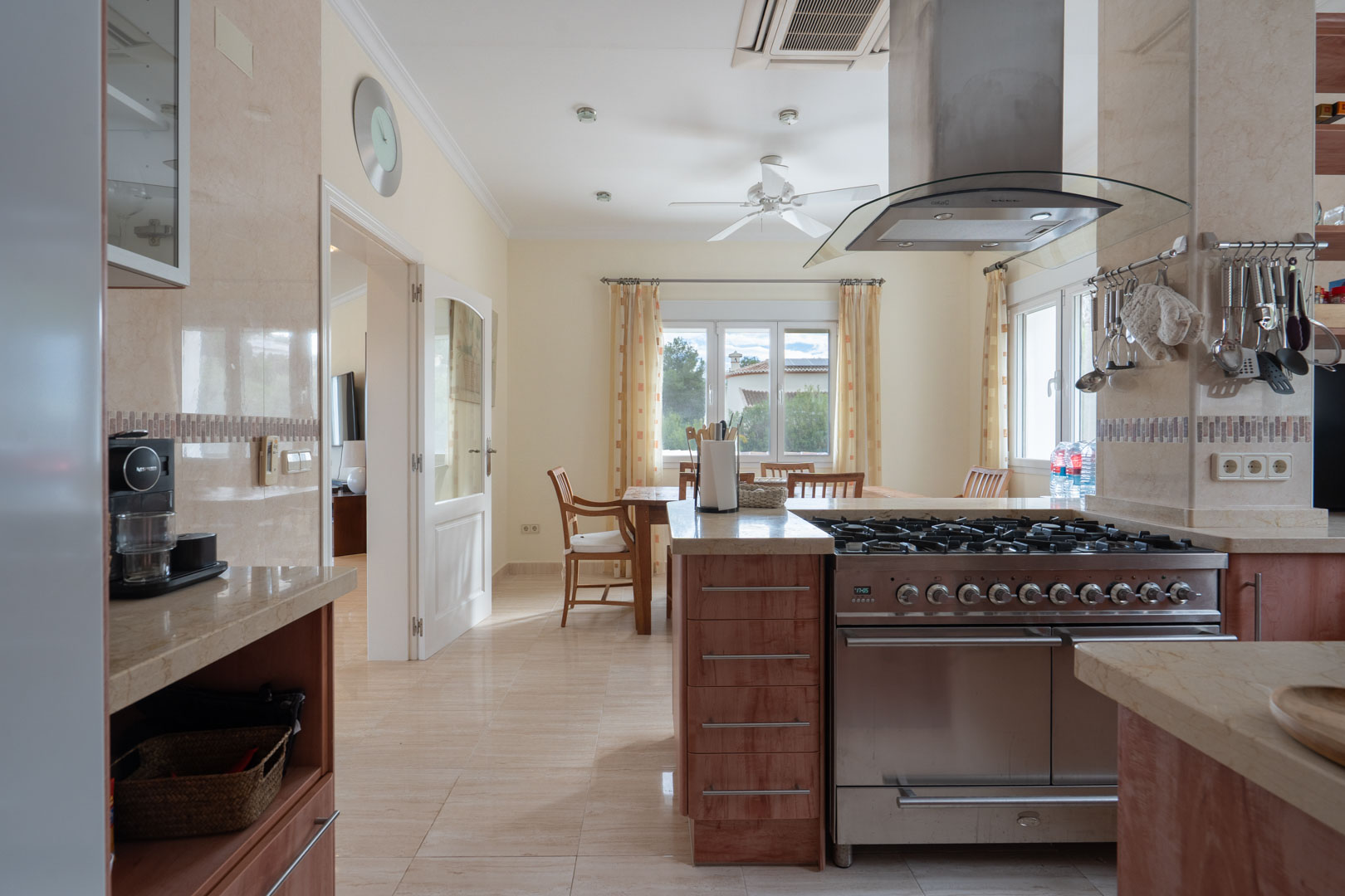 Cuisine équipée avec plans de travail en pierre, cuisinière à gaz professionnelle en inox et coin repas intégré baigné de lumière naturelle.