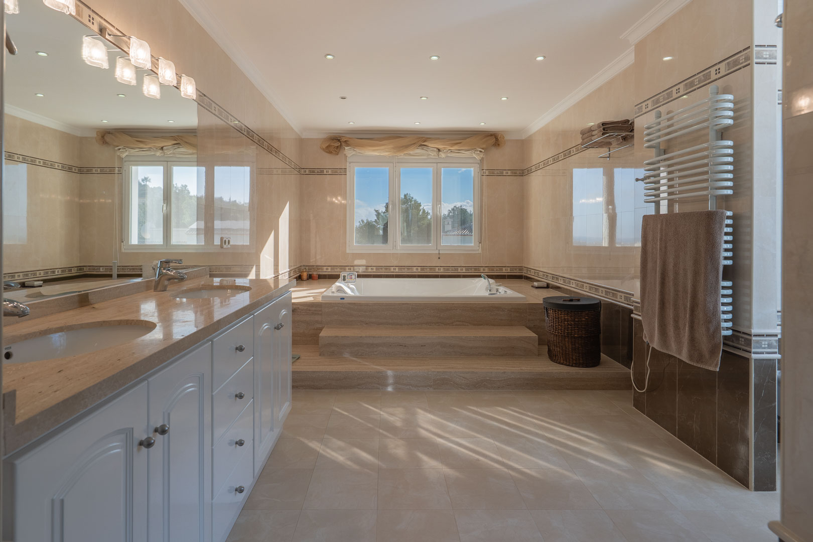 Salle de bain principale avec double vasque en marbre, baignoire d'hydromassage surélevée et finitions raffinées en grès cérame aux tons naturels.