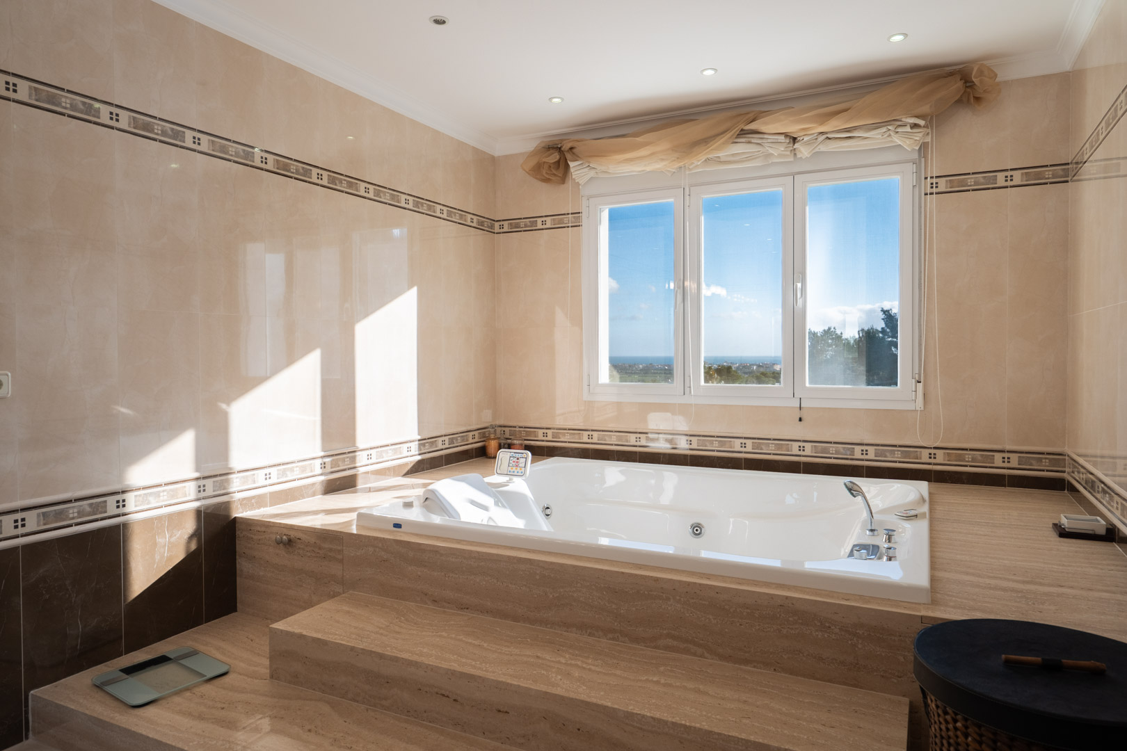 Salle de bains avec baignoire d'hydromassage encastrée dans du marbre, offrant une vue sur la mer à travers une grande fenêtre et des finitions élégantes.