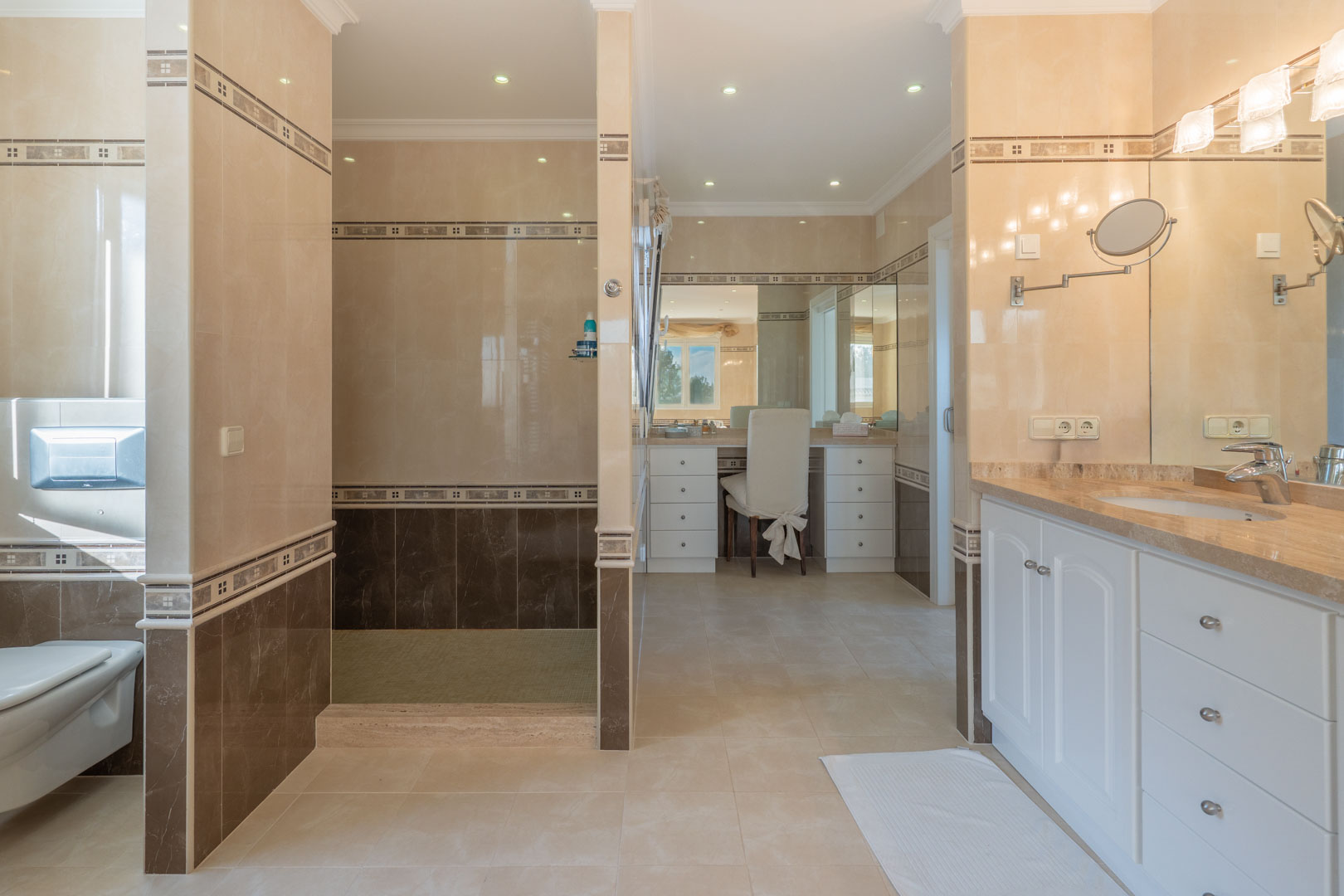 Salle de bains spacieuse avec carrelage bicolore, douche à l'italienne, coin coiffeuse et meuble vasque avec plan de travail en marbre et rangements blancs.
