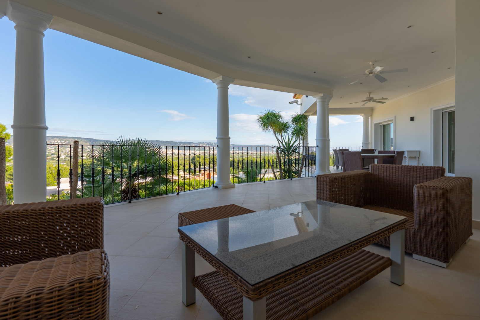 Terrasse couverte avec colonnes blanches, mobilier en osier et vue panoramique sur la vallée et le Montgó. Équipée de ventilateurs de plafond et d'un éclairage encastré.
