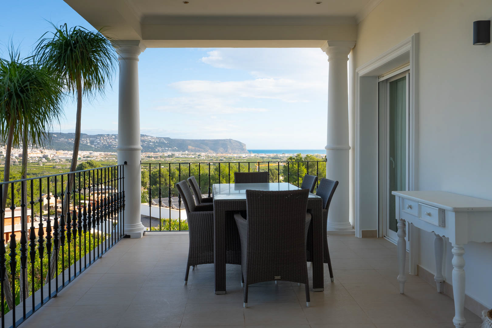 Terrasse couverte avec colonnes classiques et garde-corps en fer forgé, offrant un coin repas extérieur et une vue panoramique sur la mer Méditerranée.