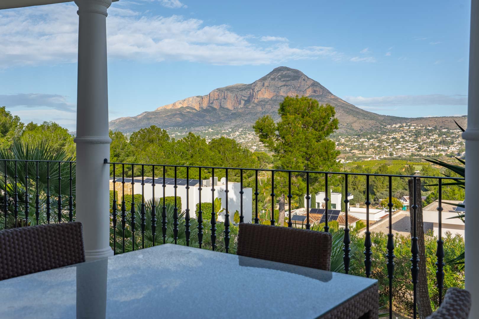 Terrasse couverte avec espace repas extérieur et garde-corps en fer forgé, offrant une vue panoramique sur le massif du Montgó.