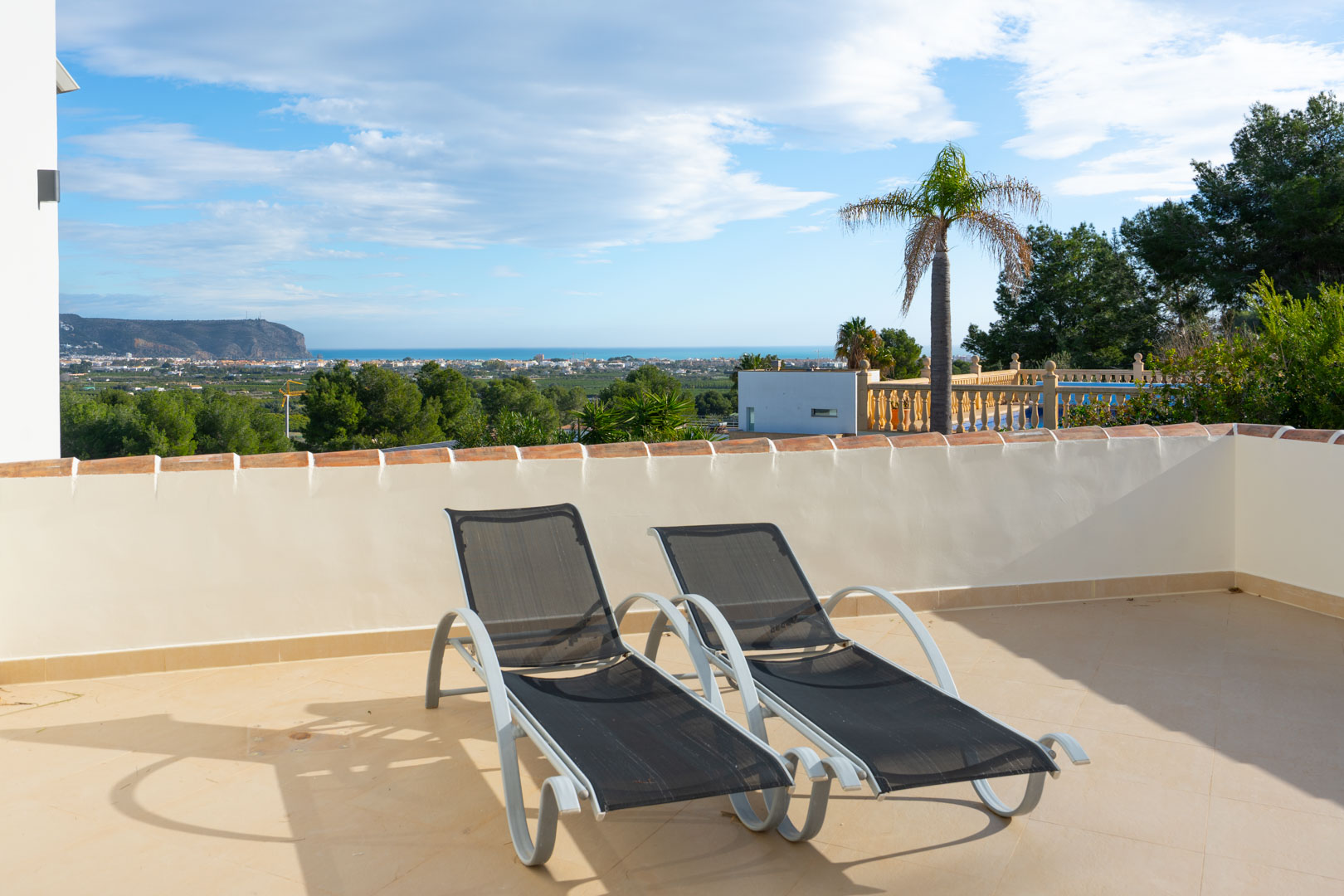 Terrasse solarium avec deux chaises longues modernes, offrant une vue panoramique sur la mer Méditerranée et la silhouette du Montgó.