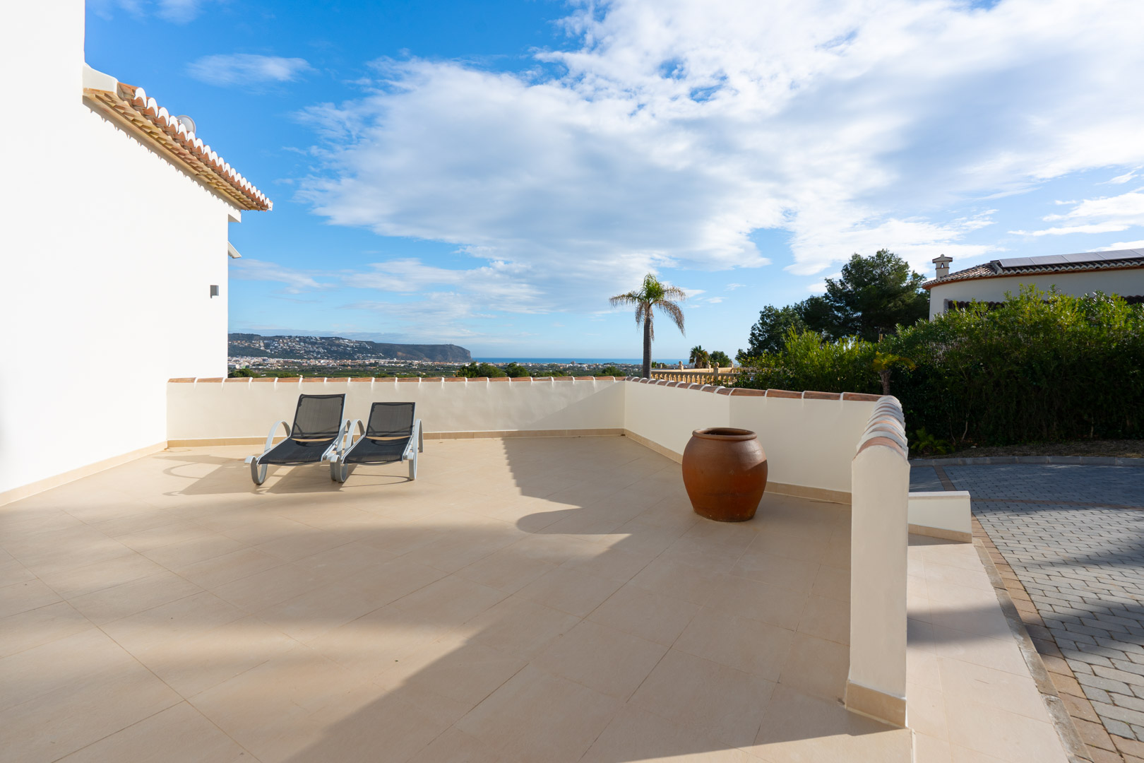 Terrasse solarium spacieuse avec carrelage en céramique, chaises longues et vue panoramique sur la côte méditerranéenne et le paysage environnant.