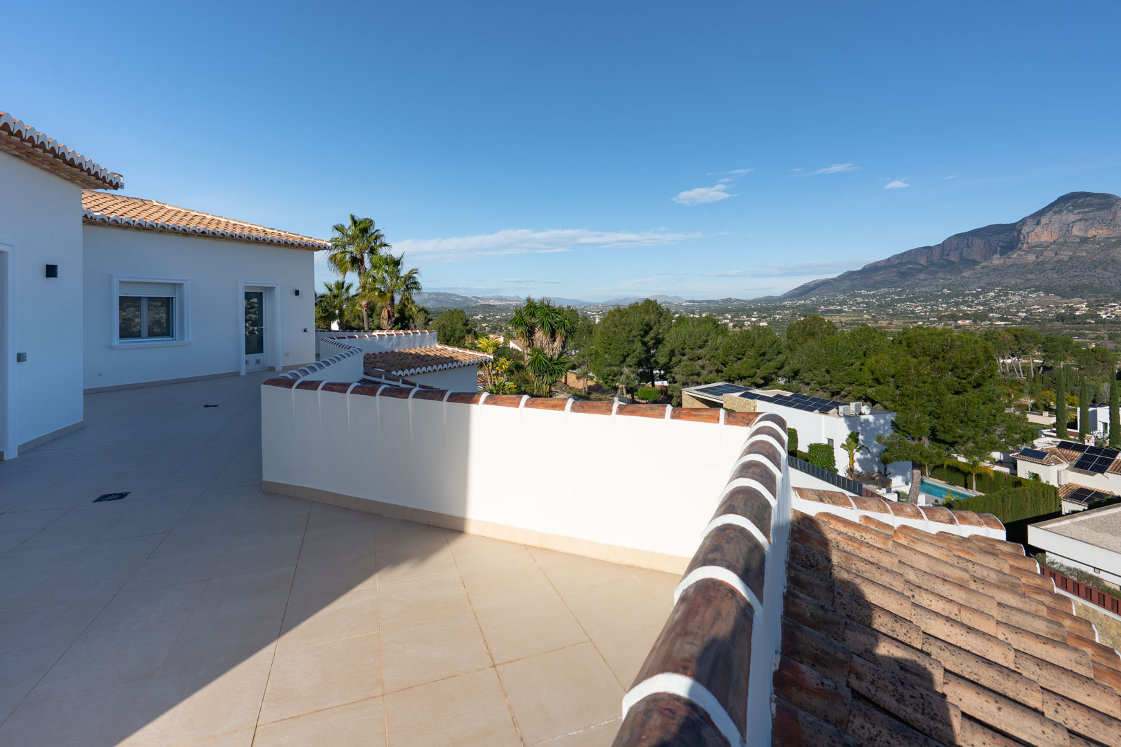 Terrasse supérieure avec carrelage en céramique beige offrant une vue panoramique sur le massif du Montgó et le paysage environnant.