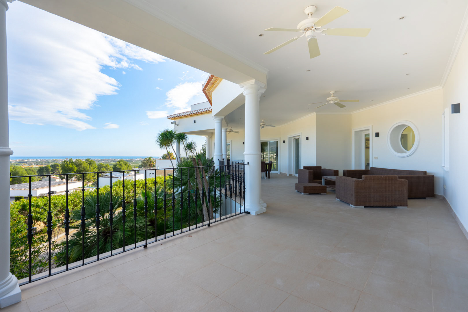 Vaste terrasse couverte avec colonnes blanches, mobilier en rotin et vue panoramique sur la mer Méditerranée et le paysage côtier.