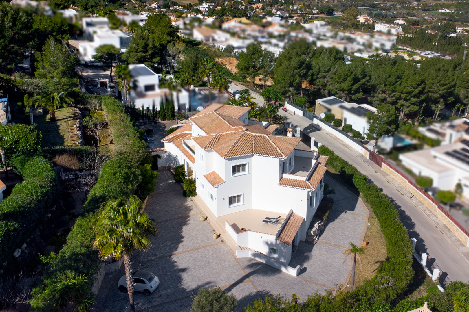 Vue aérienne de la villa blanche aux toits de tuiles, montrant sa vaste entrée pavée et ses terrasses privées entourées d'une végétation méditerranéenne.