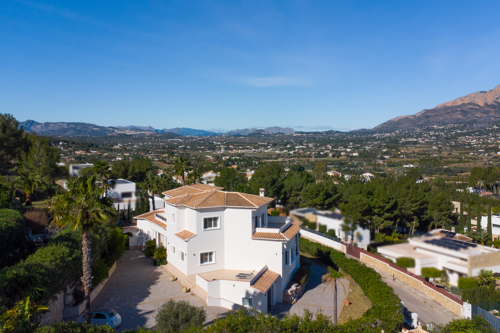 Vue extérieure surélevée de la villa blanche aux toits de tuiles, mettant en valeur sa large entrée pavée et ses vues panoramiques sur la vallée et le Montgó.