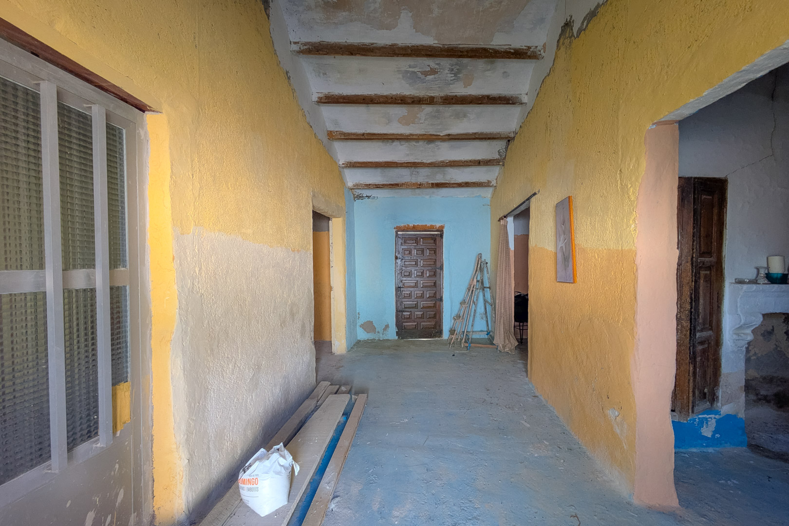 Couloir intérieur avec de hauts plafonds à poutres en bois apparentes et des murs rustiques, illustrant le caractère authentique et le potentiel de rénovation.