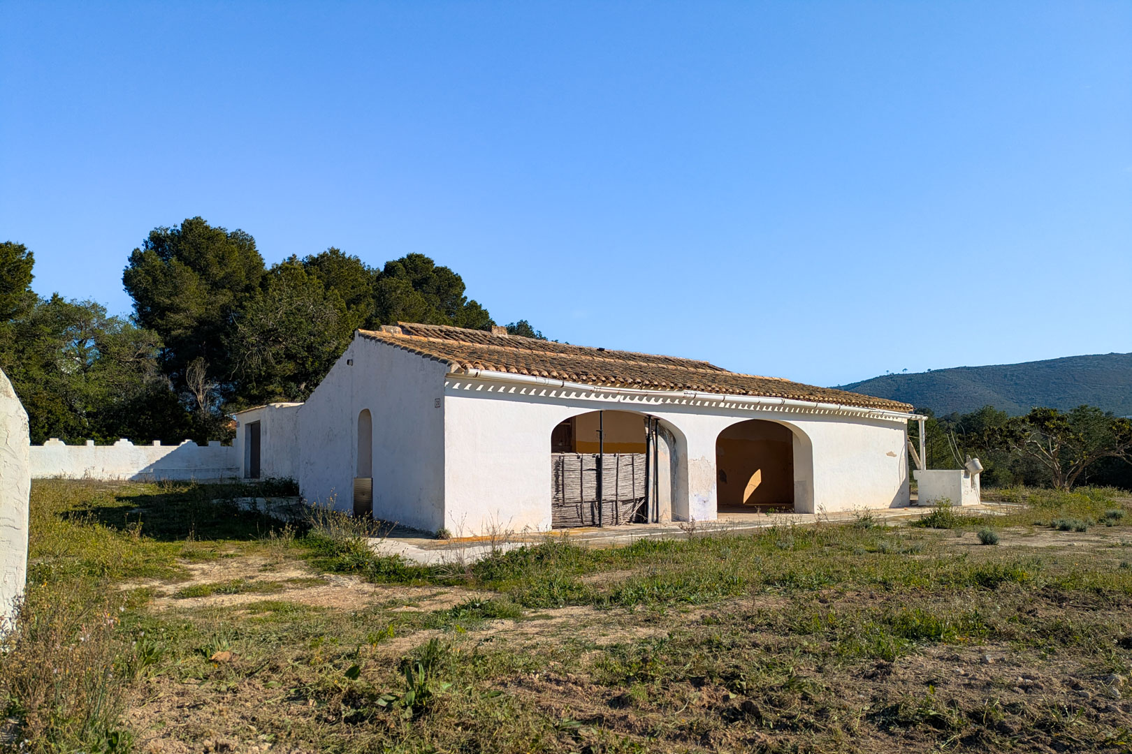 Façade de la finca traditionnelle avec naya à arches et toit en tuiles, située sur un vaste terrain rustique entouré de nature.