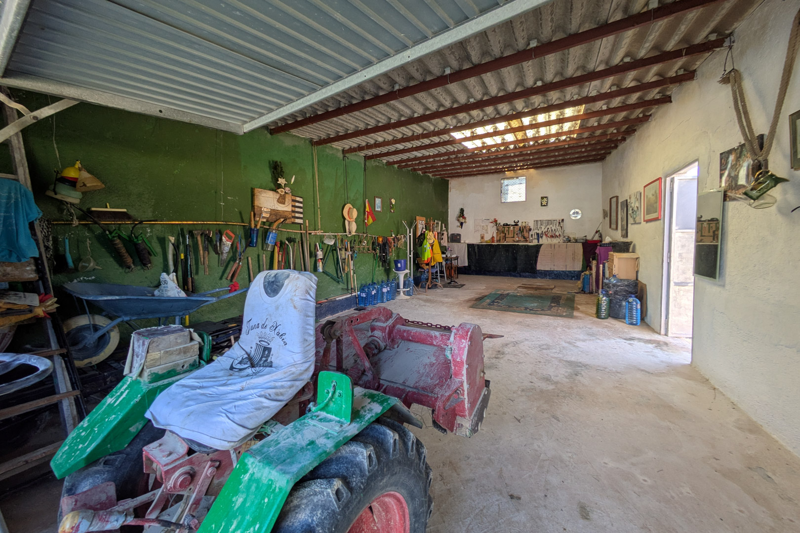 Grand atelier ou espace de stockage avec sol en béton et hauts plafonds à poutres métalliques, idéal pour les machines agricoles et l'outillage.