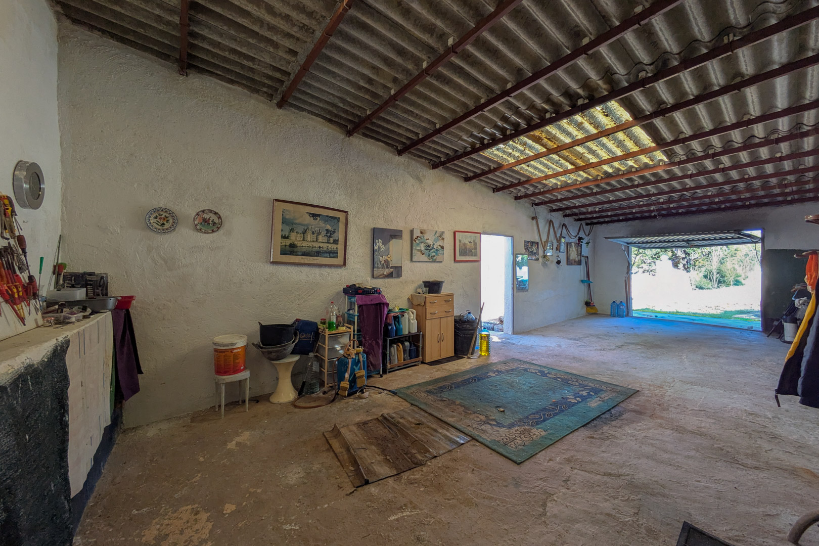 Grand garage ou atelier avec sol en béton, murs blanchis à la chaux et hauts plafonds dotés d'un puits de lumière naturelle.