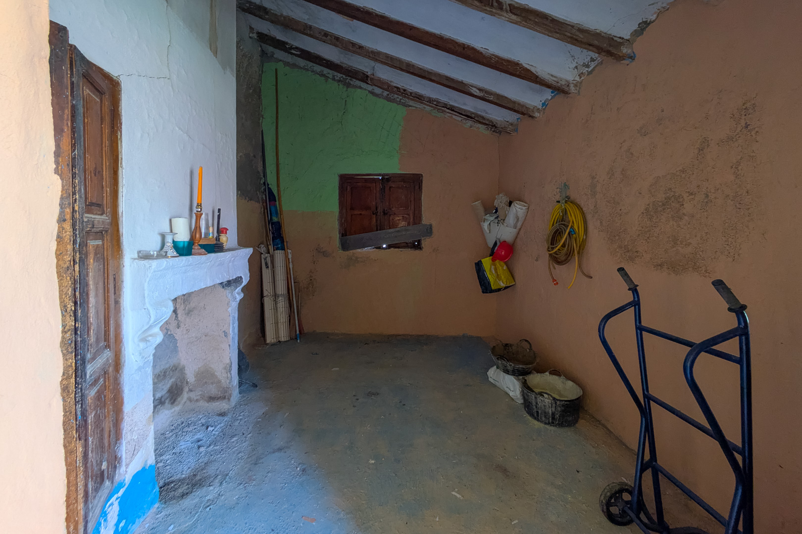Intérieur rustique avec cheminée traditionnelle, plafond incliné à poutres apparentes et murs texturés, offrant un grand potentiel de rénovation.