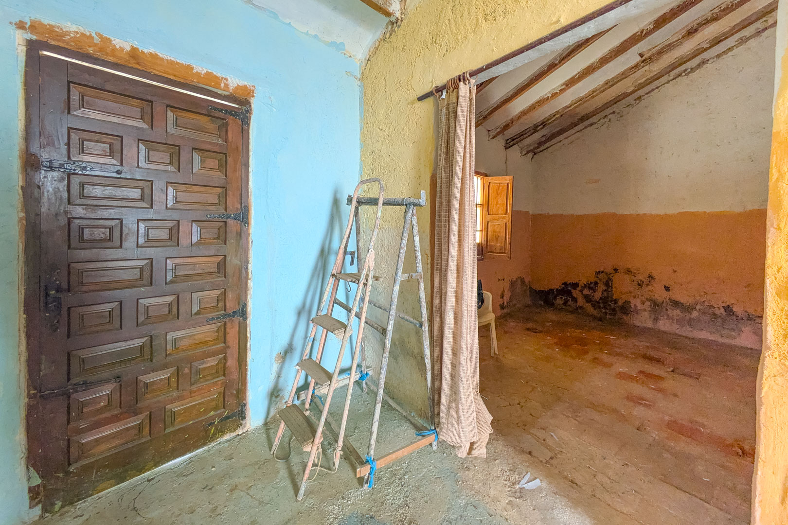 Intérieur rustique avec porte en bois sculpté, murs colorés et poutres apparentes, illustrant le caractère authentique et le potentiel de rénovation.