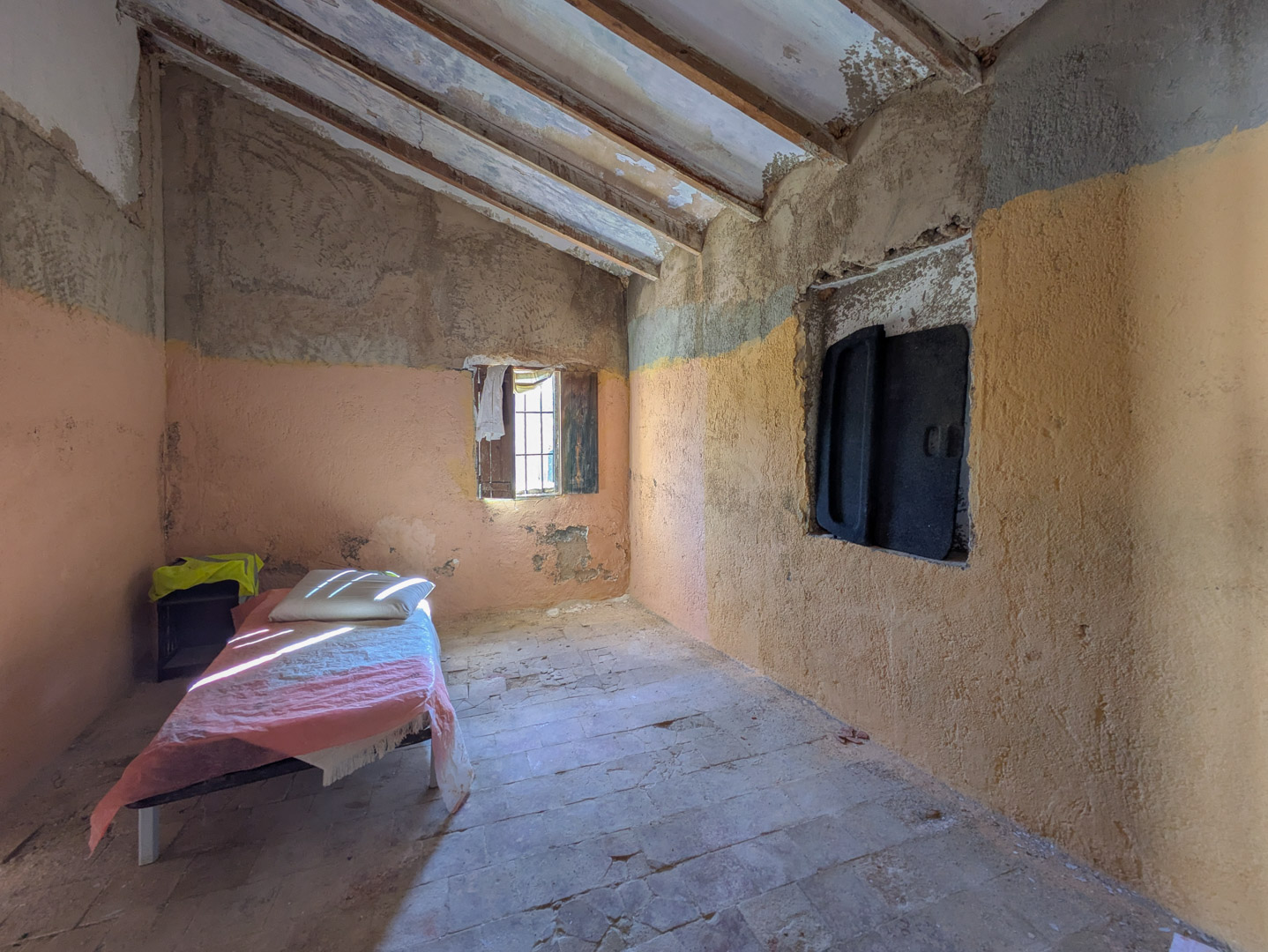 Intérieur rustique avec poutres en bois apparentes, sol en terre cuite d'origine et murs à rénover bénéficiant d'une lumière naturelle.