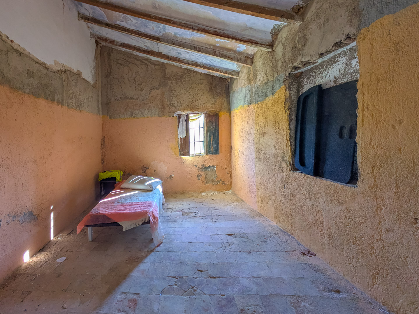 Pièce intérieure avec plafonds inclinés à poutres apparentes, sol en terre cuite d'origine et murs en plâtre rustique nécessitant une rénovation totale.