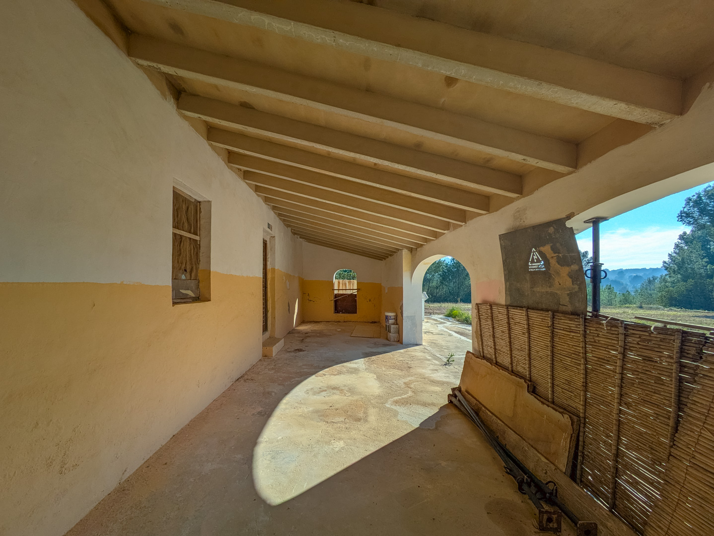 Porche couvert traditionnel avec poutres en bois apparentes et murs ocre, offrant une vue sur la nature environnante de Jávea.