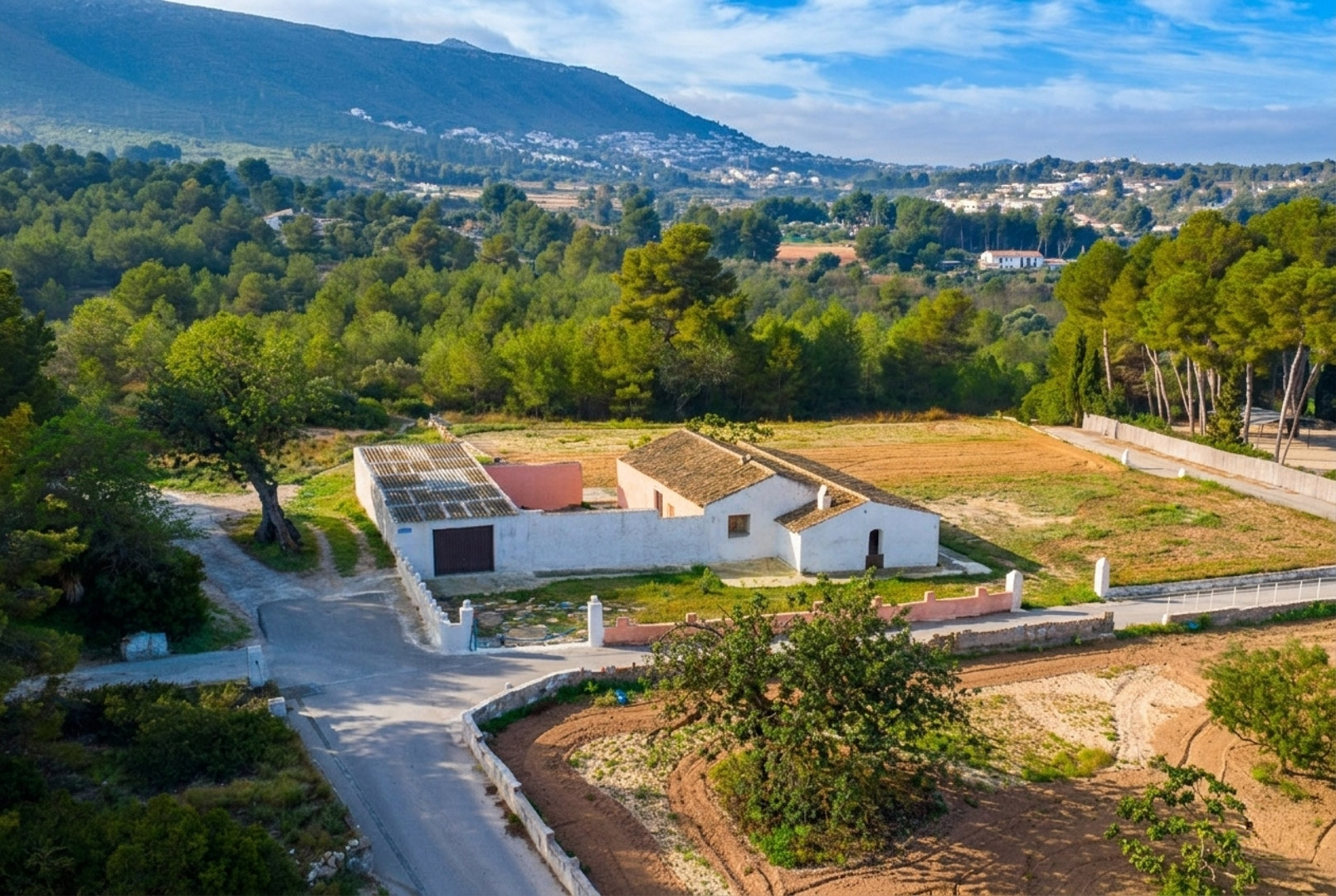 Vue aérienne de la finca traditionnelle aux murs blancs et toits de tuiles, implantée sur un vaste terrain plat entouré de pinèdes et de montagnes.
