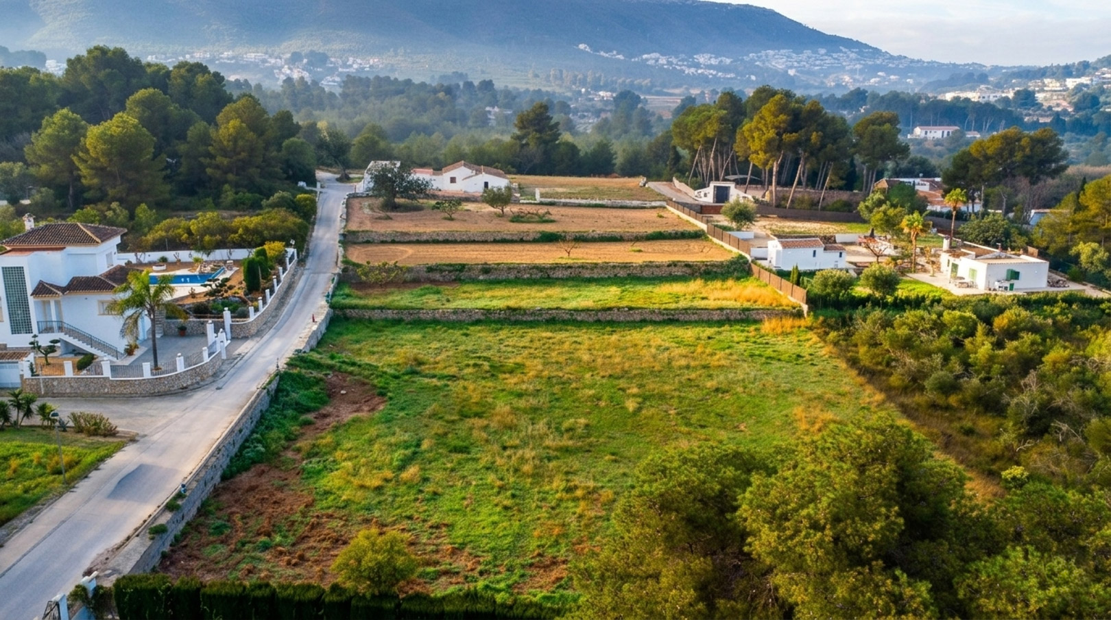 Vue aérienne du terrain rustique avec ses restanques en pierre, entouré de forêts de pins avec les montagnes de Jávea en arrière-plan.