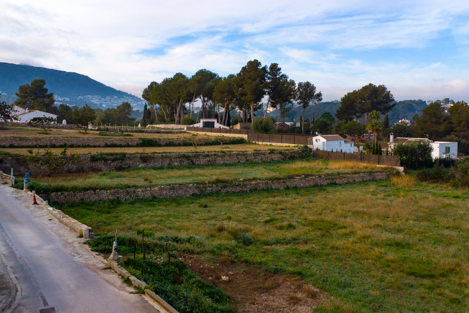 Vue des terrasses en pierre sèche sur le vaste terrain rustique, entouré de végétation méditerranéenne avec les montagnes en arrière-plan.