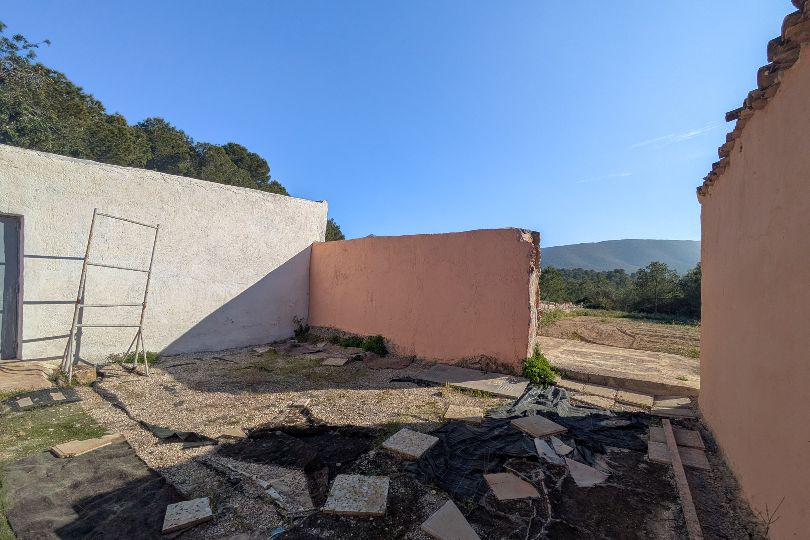 Vue d'une structure extérieure avec des murs en crépi blanc et terre cuite, offrant une perspective sur le terrain naturel et les collines environnantes.