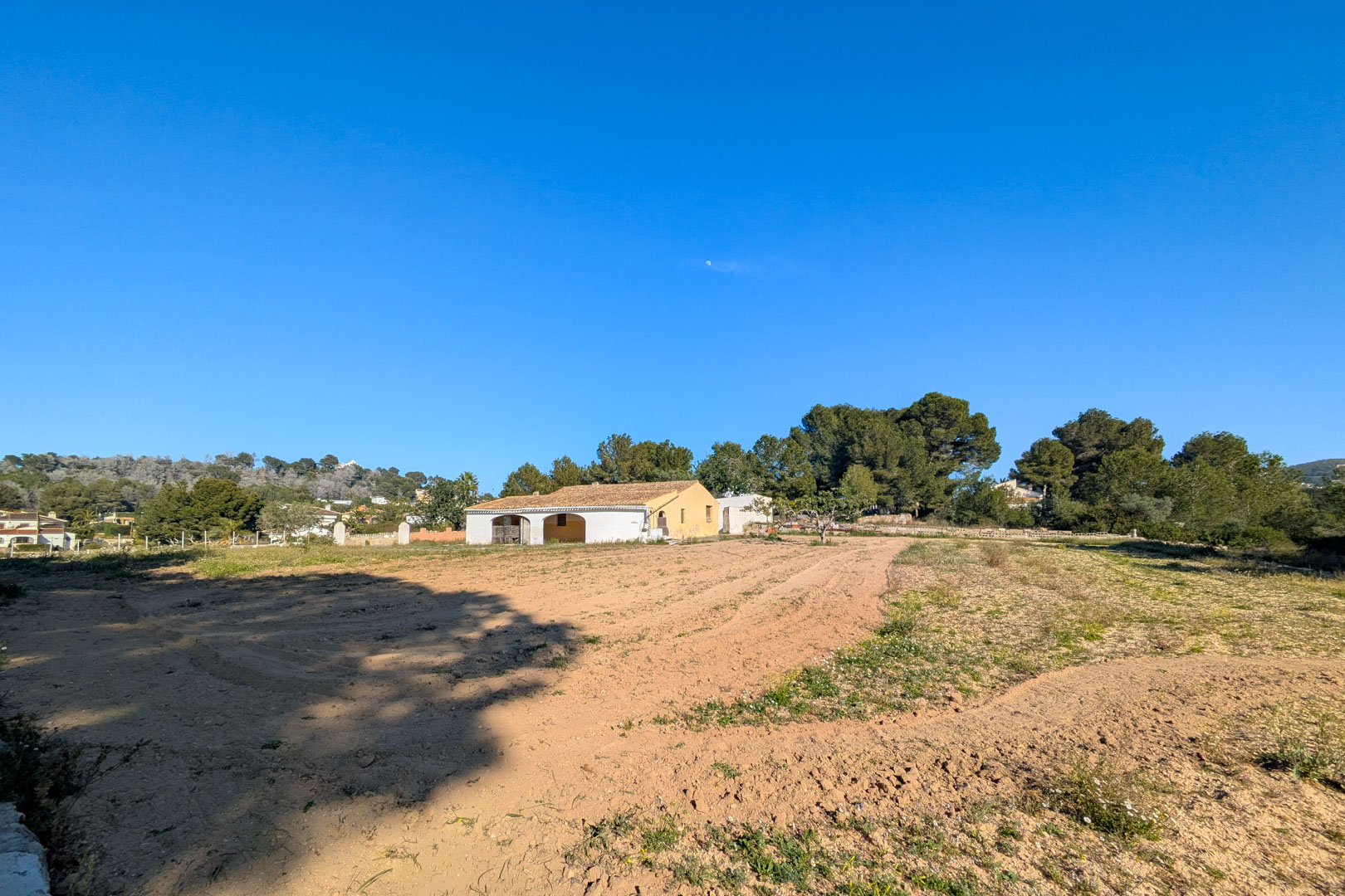Vue extérieure de la finca traditionnelle avec porche à arches, située sur un grand terrain rustique plat entouré de pins et de paysages naturels à Jávea.