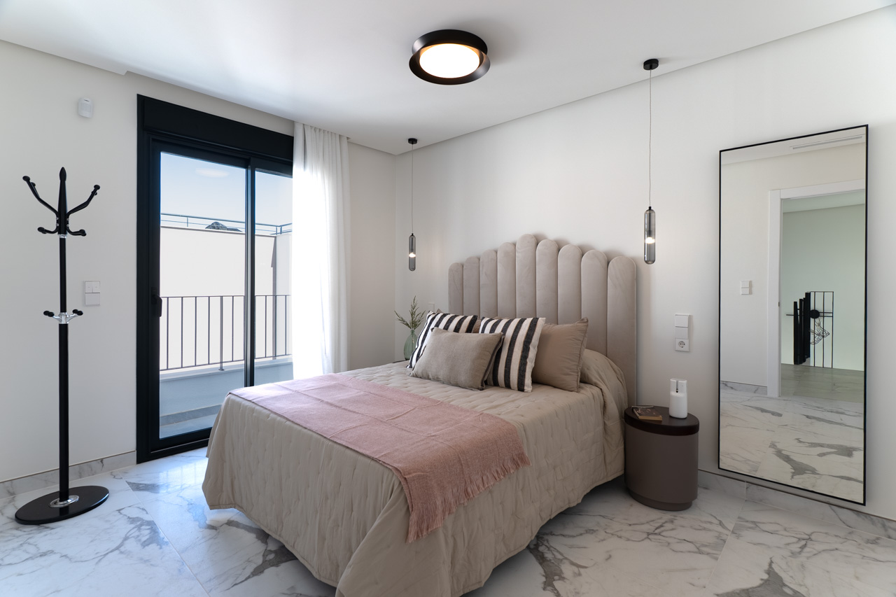 Chambre double avec sol en grès cérame effet marbre, tête de lit capitonnée et accès direct à une terrasse privée par une baie vitrée à cadre noir.