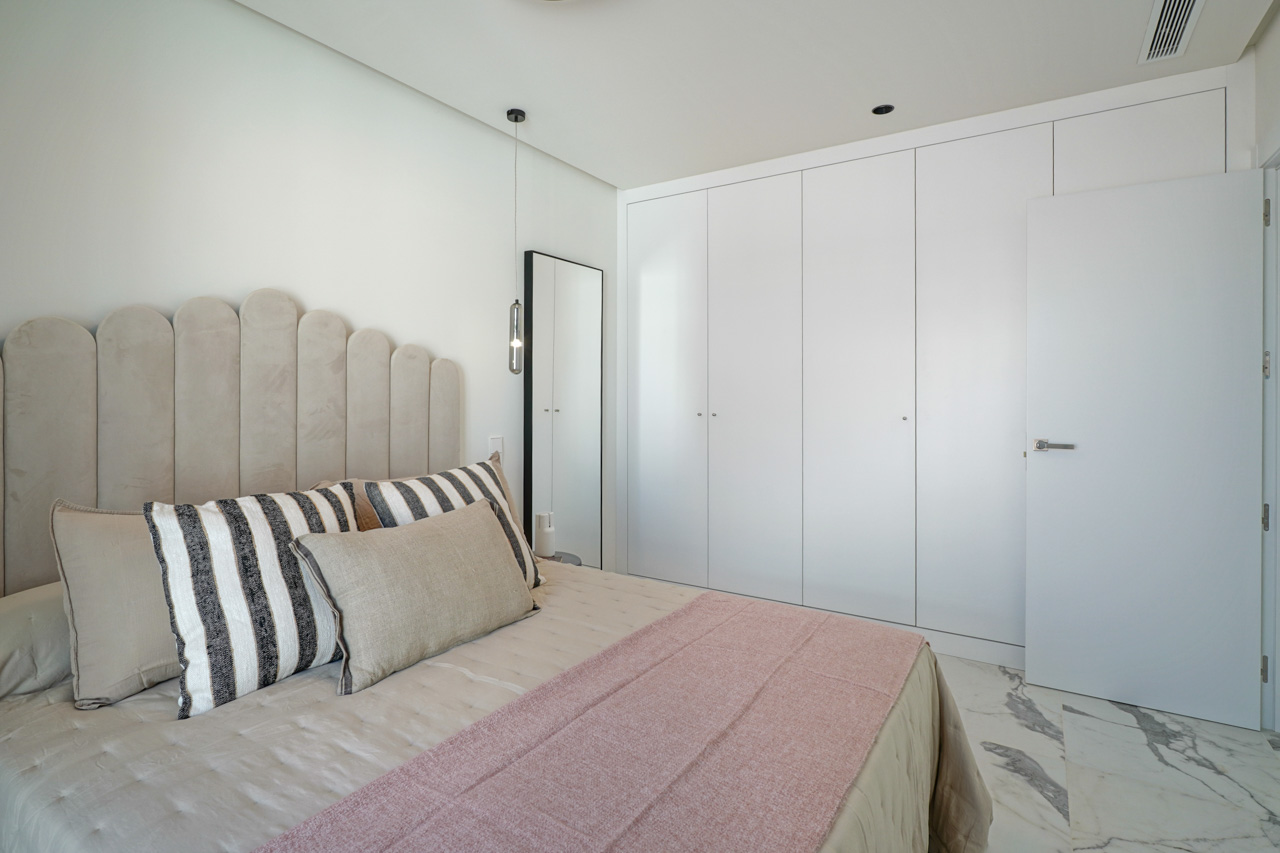 Chambre moderne avec placards intégrés blancs, sol en marbre veiné et une tête de lit capitonnée au design arrondi avec éclairage suspendu.