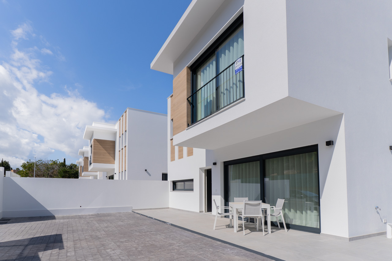 Façade moderne aux lignes épurées avec accents en bois, terrasse pavée et coin repas extérieur devant de grandes baies vitrées coulissantes.
