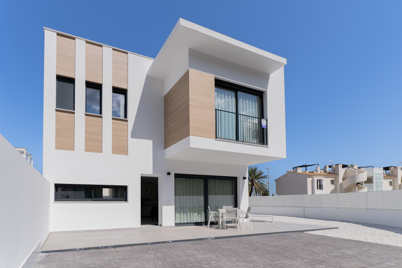 Façade moderne avec parement aspect bois, terrasse pavée équipée d'un salon de jardin et grandes baies vitrées aux menuiseries noires.
