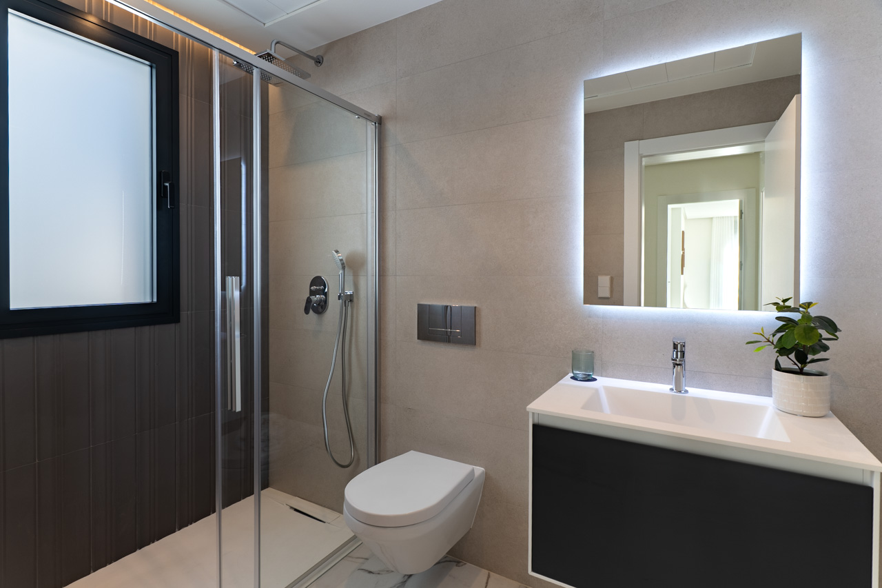 Salle de bains moderne avec douche à l'italienne, paroi vitrée, WC suspendu et meuble vasque surmonté d'un miroir à éclairage LED intégré.
