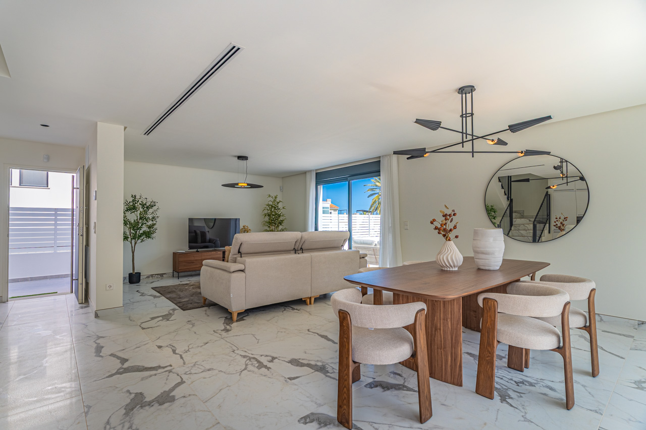 Salon-salle à manger à aire ouverte avec sol en grès cérame effet marbre, mobilier en bois moderne et accès direct à la terrasse ensoleillée.