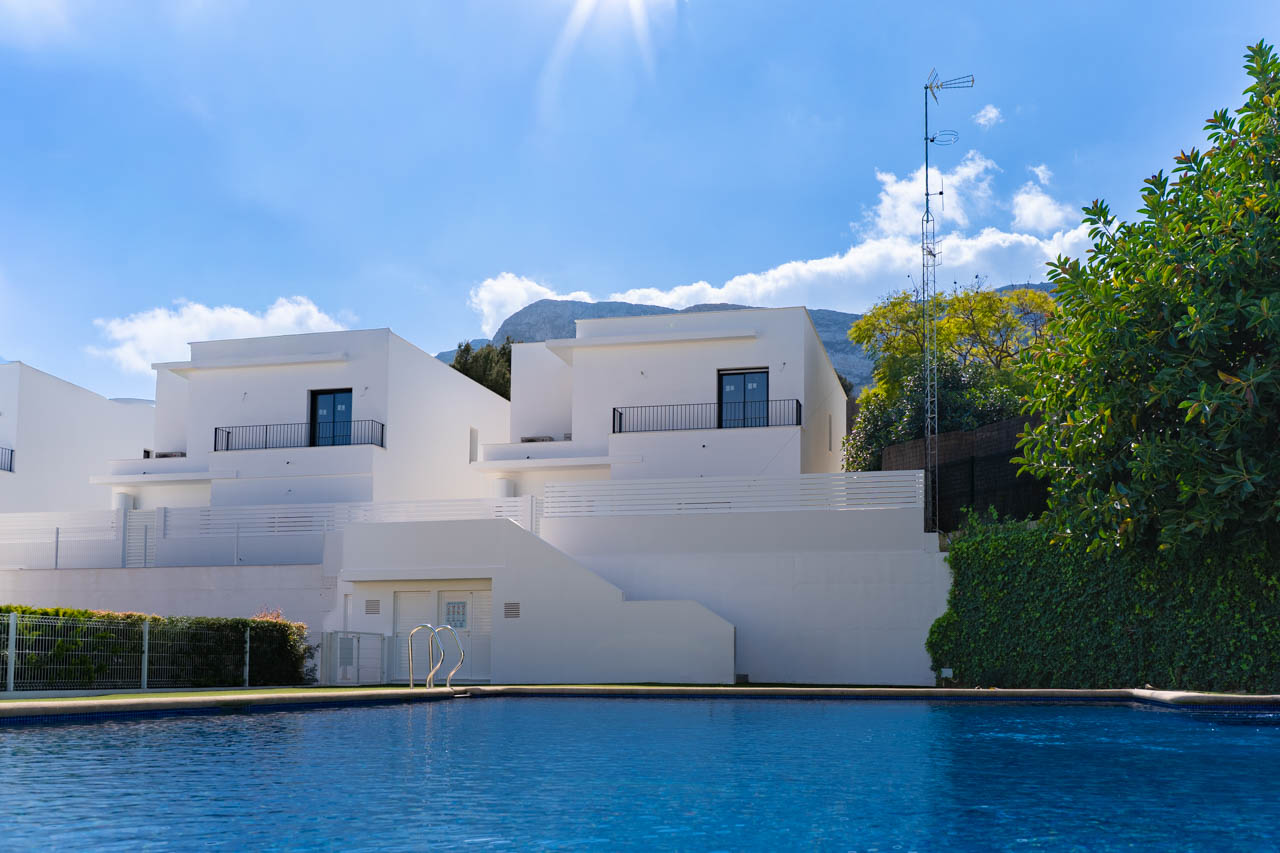 Vue des villas modernes depuis la piscine commune, présentant des façades blanches épurées avec le massif du Montgó en arrière-plan.