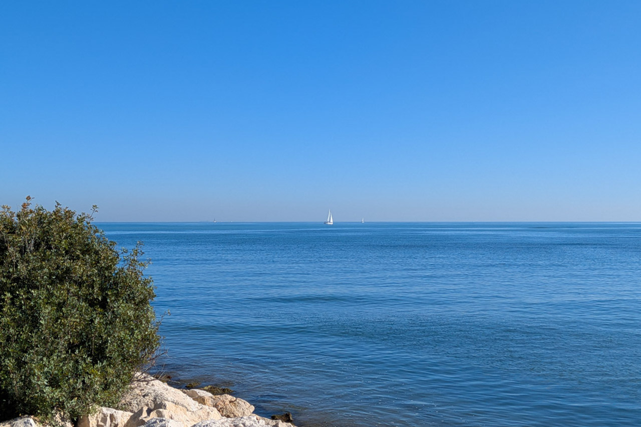 Vue panoramique sur la mer Méditerranée depuis la côte rocheuse de Dénia, avec des voiliers à l'horizon sous un ciel bleu azur.