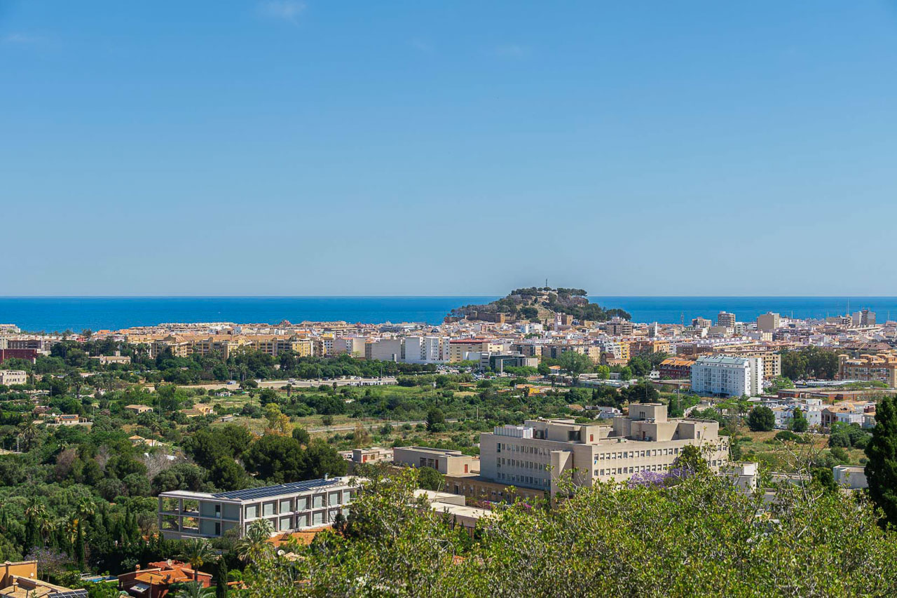 Vues panoramiques sur Dénia, incluant le château historique et la mer Méditerranée à l'horizon. La perspective élevée souligne la proximité du centre-ville et de la côte.