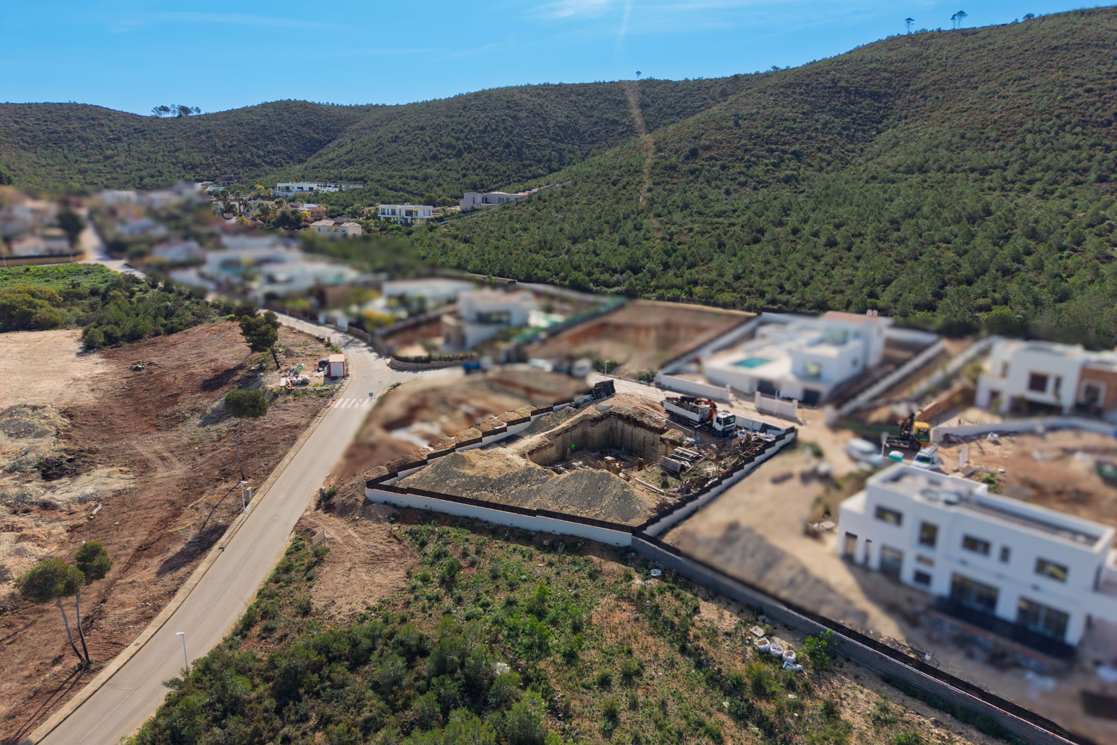 Vue aérienne du terrain en phase d'excavation et de fondation, situé dans l'urbanisation Valsol, entouré de collines verdoyantes et de villas contemporaines.
