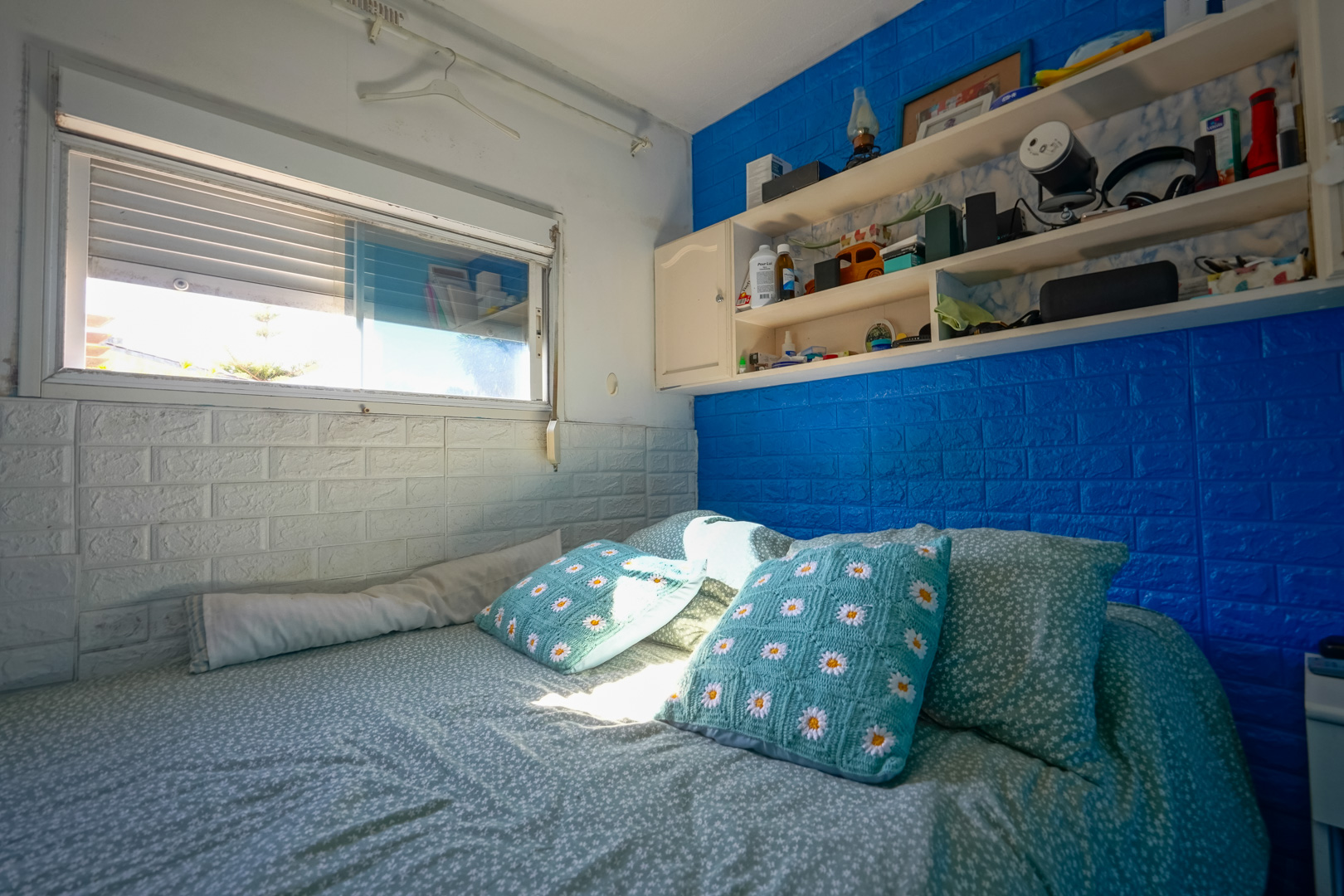 Chambre de l'unité préfabriquée avec murs à effet brique bleu et blanc, étagères intégrées et lumière naturelle.