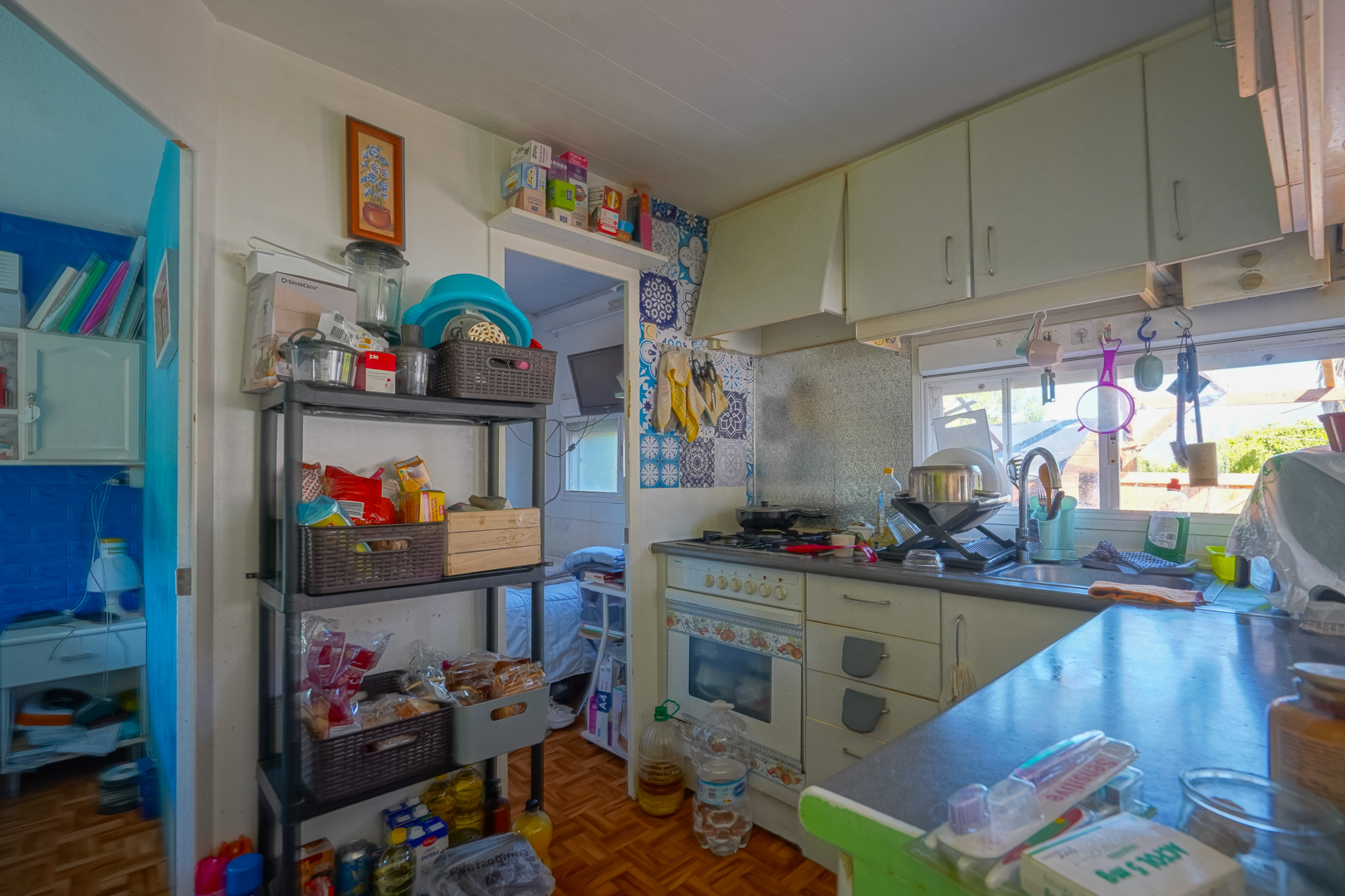 Cuisine compacte de la maison d'amis avec armoires blanches, crédence en mosaïque bleue et étagères de rangement, bénéficiant d'une lumière naturelle constante.